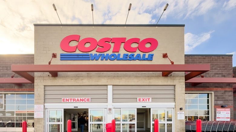The storefront of Costco with a clearly marked entrance and exit. A red sign reads Costco, while underneath a blue sign reads wholesale.