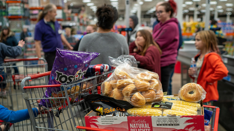 A Costco cart sits in front of a blurred family crowded in a circle talking.