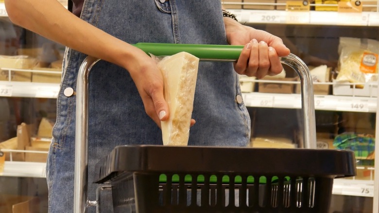 Close-up of a young woman's hands putting a package of cheese into a shopping cart