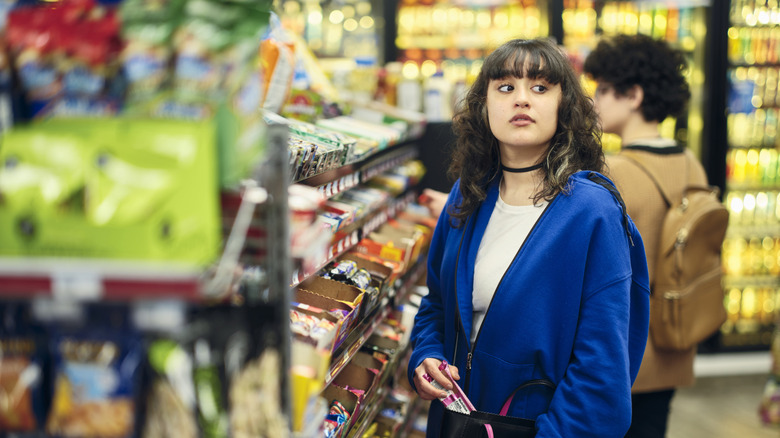 A young woman shoplifting or stealing merchandise from a grocery store aisle