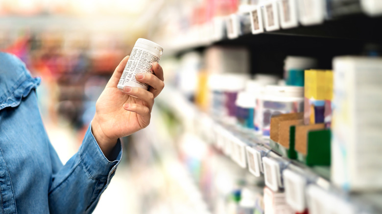 Customer in pharmacy aisle holding medicine bottle at grocery store