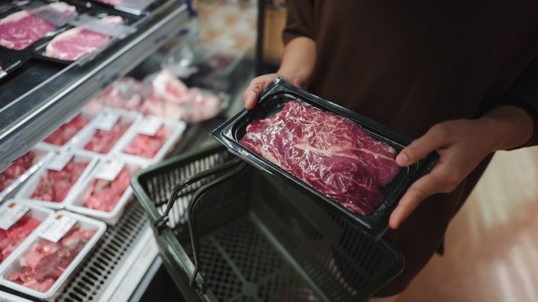 Woman holding a tray filled with fresh red meat while browsing the supermarket
