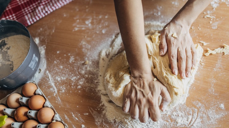 A woman kneads dough on a wooden kitchen table