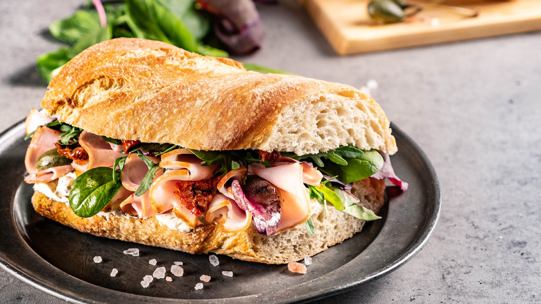 Sub sandwich with vegetables sits on a black plate