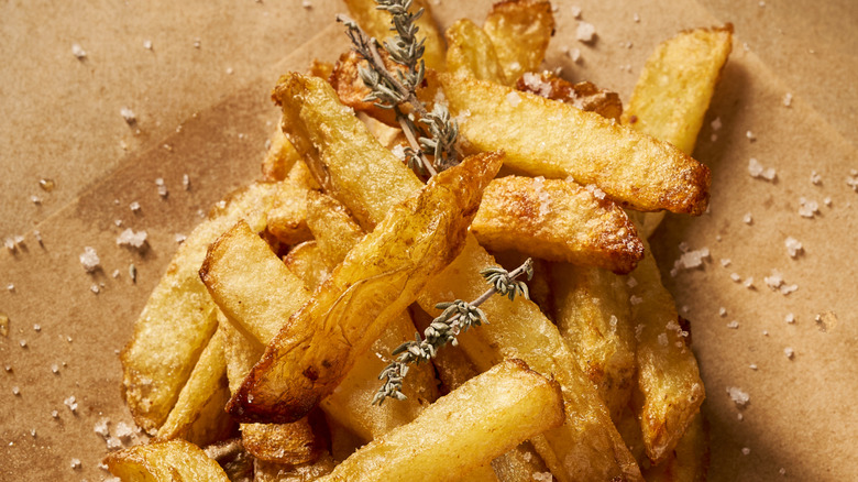 A pile of thick, salted french fries with sprigs of thyme on paper