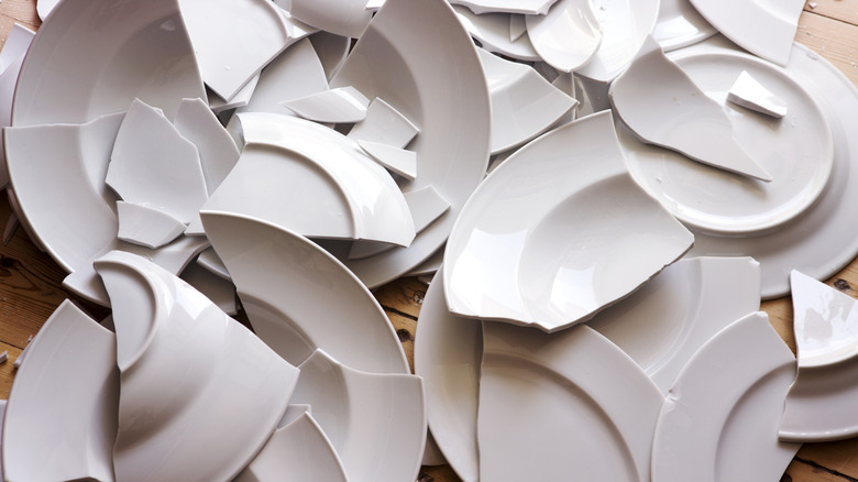 Several smashed white plates sitting on a hardwood floor.