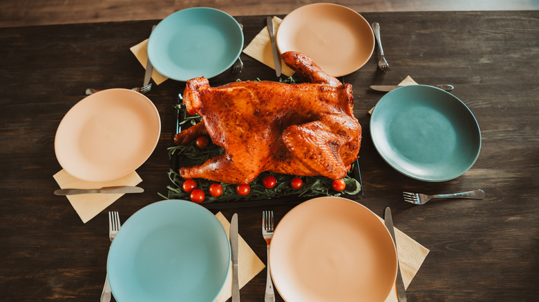 A cooked bird, surrounded by cutlery and plates in a circle.