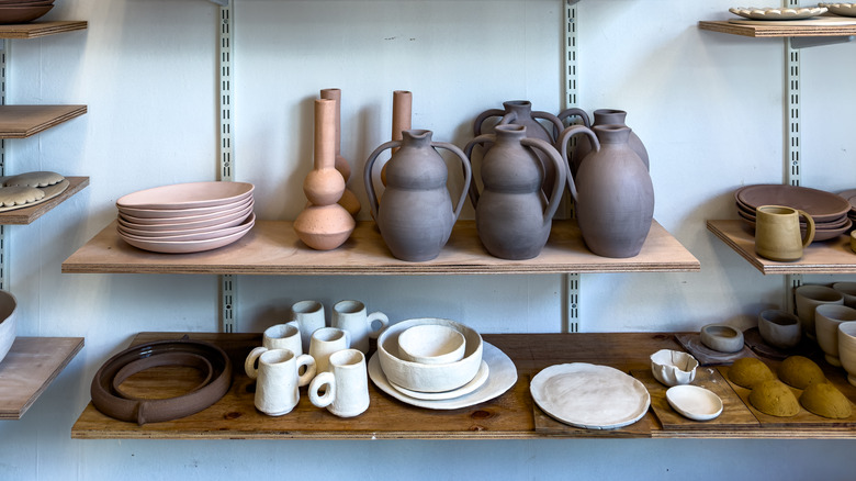 Unfired clay vases, and dishware rest on a wooden rack.