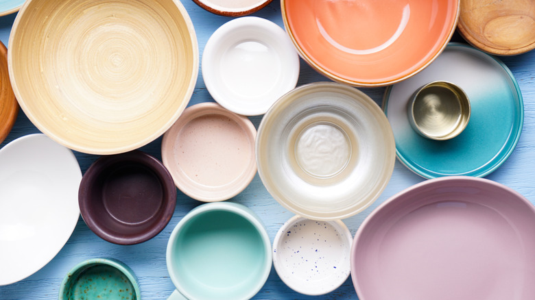A birdseye view of several different sizes and colors of bowls and cups on a blue table.