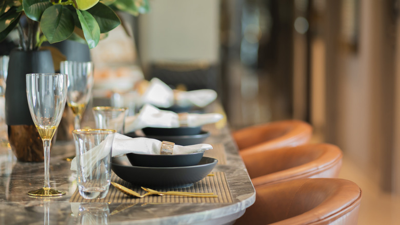 A marble dinner table set with dishware. Leather bar stools are lined up for diners.