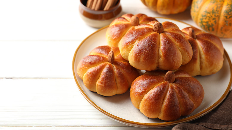 Tasty pumpkin shaped buns and ingredients on white wooden table, close-up