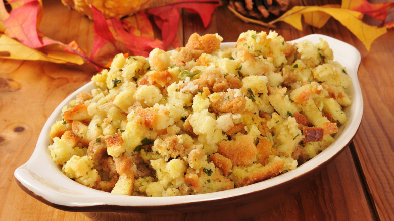 A small casserole dish of cornbread stuffing on a rustic wooden table with autumn leaves and pine cones