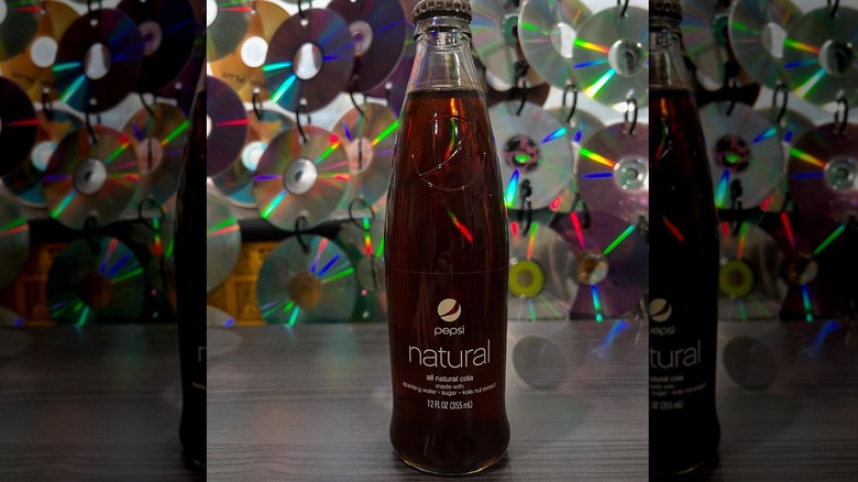 Closeup of a glass bottle of Pepsi Natural on table with background of hanging CDs