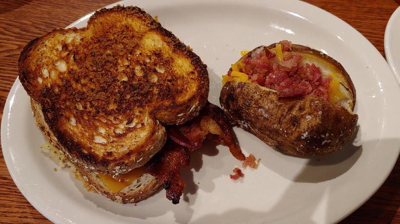 A sandwich and baked potato on a white oval plate at Cracker Barrel