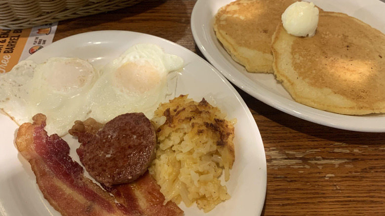 Two plates of food diagonal each other, one with two pancakes, the other with bacon and eggs at Cracker Barrel