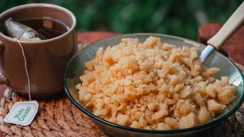 A cup with a mate tea bag rests beside a bowl of food with a spoon in it.