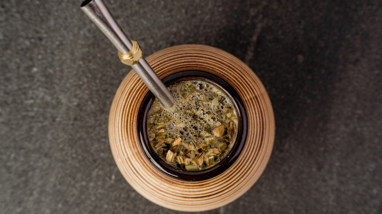 Birds-eye view of brewed mate leaves in a cup with a bombilla sticking out.