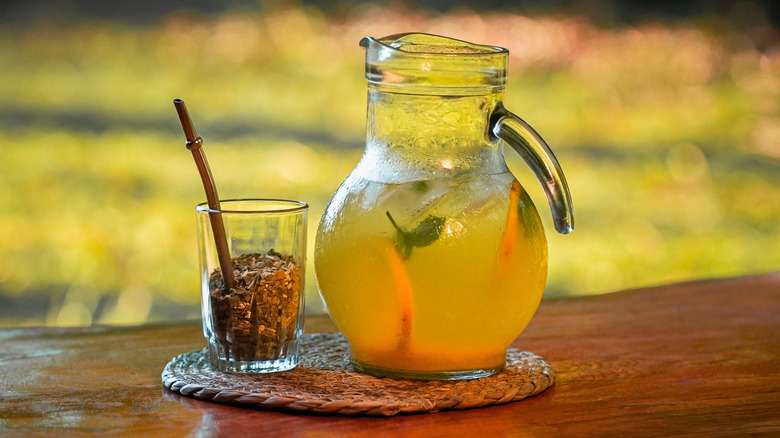 A glass of mate with a bombilla inside rests beside a pitcher of juice.