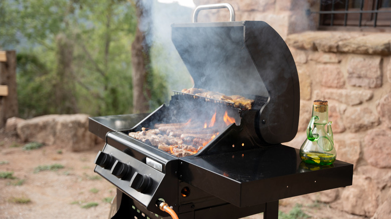 Open barbecue grill with smoke and fire cooking meat in a backyard patio
