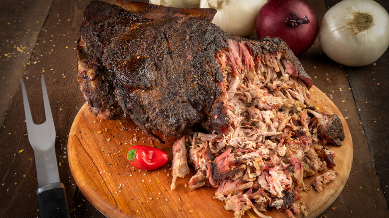 Styled shot of a Boston butt roast sitting on a wood platter resting on a rustic wood surface