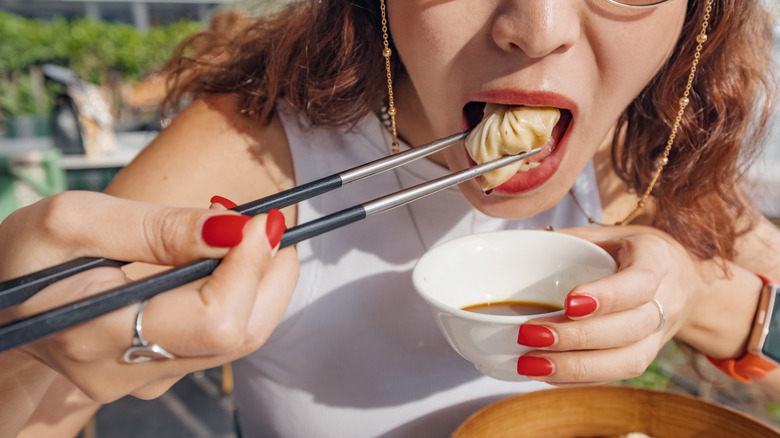 Close-up of a woman popping a dumpling into her mouth with chopsticks