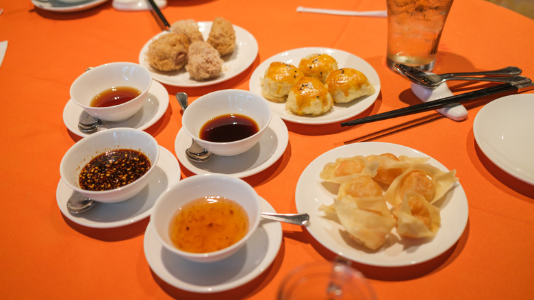 An orange table topped with cups of tea, plates of dumplings, and dishes of various dipping sauces