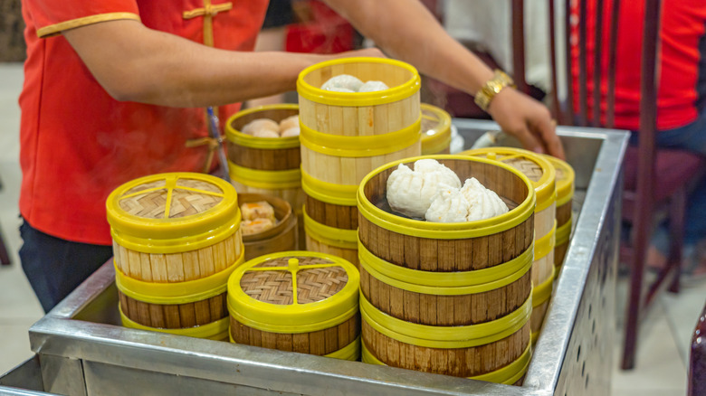 An unidentifiable server in traditional Chinese dress serving dim sum in bamboo steamer boxes