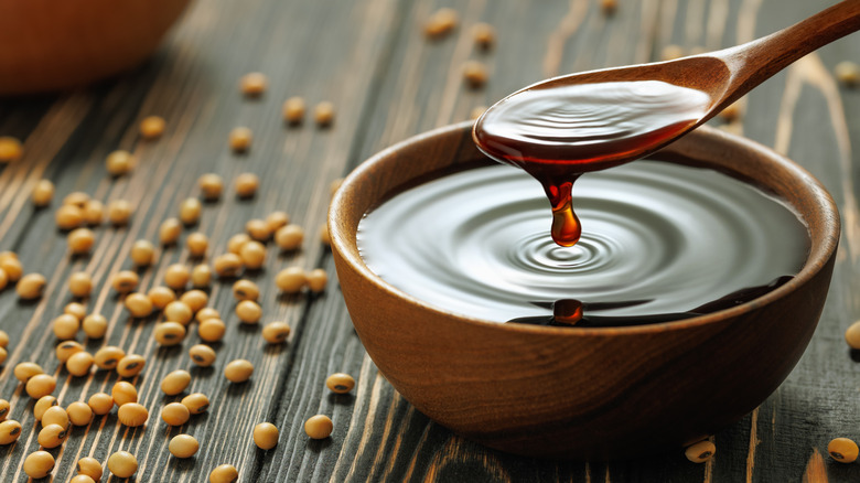 Soy sauce in a bowl with a wooden spoon surrounded by soy beans