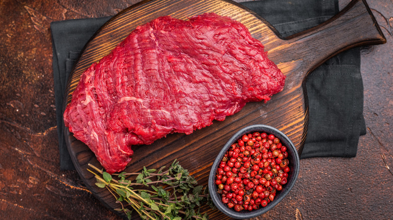 Raw flank steak on a cutting board with herbs and spices