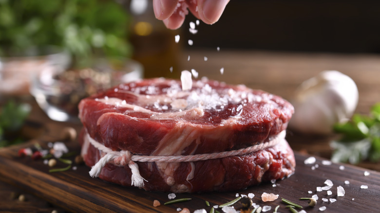 Hand sprinkling salt on fresh raw beef meat on a cutting board