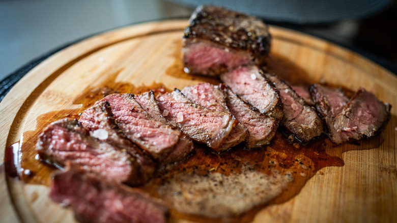 A juicy beef steak sliced and resting on a round wooden cutting board, sprinkled with coarse sea salt