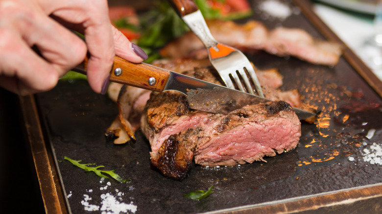 Hands holding knife and fork cutting grilled beef steak