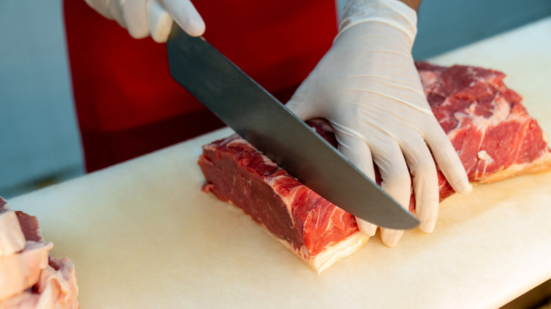 A butcher wearing protective gloves cutting slices of steak
