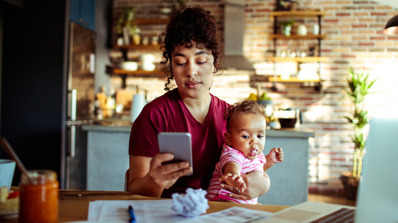 Close up of a mother using a phone with her daughter while having breakfast and doing bills