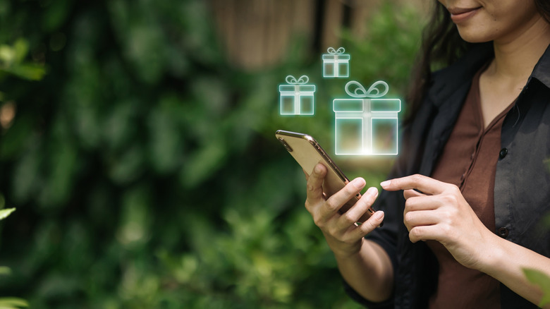 A woman holds a mobile phone with floating virtual gift box holograms