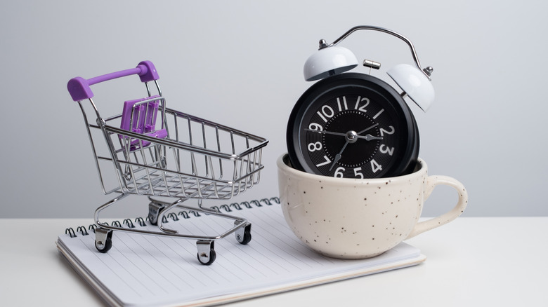 Alarm clock in a coffee mug and a shopping cart on a spiral bound notebook
