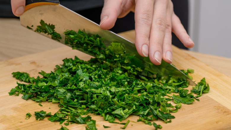 Parsley being cut on a cutting board with a chef's knife