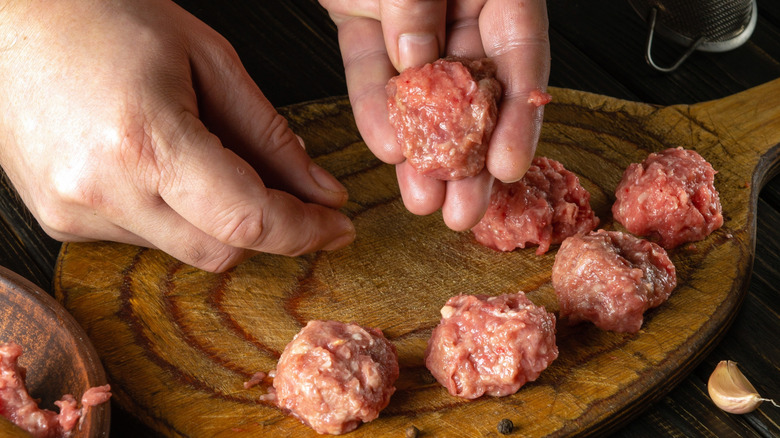 Hands shaping raw meatballs on a wooden cutting board