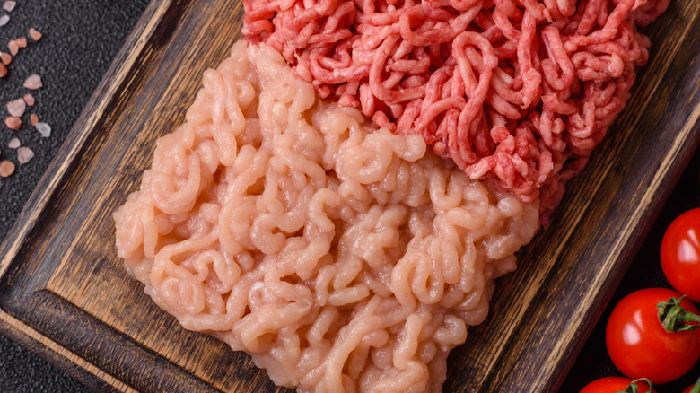 Different types of ground meat sitting on a wooden cutting board