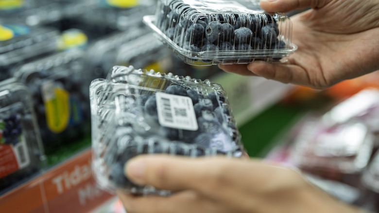 Close-up of a shopper's hands holding two plastic containers of fresh blueberries upside down