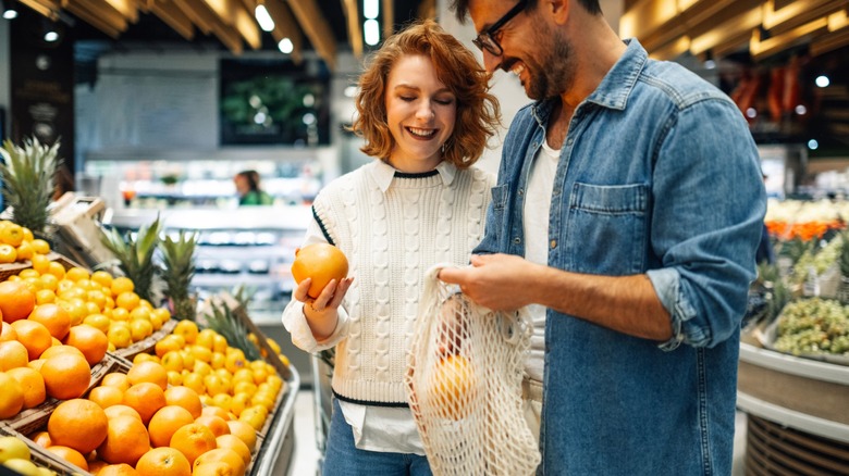 Young smiling couple buying fresh oranges at supermarket
