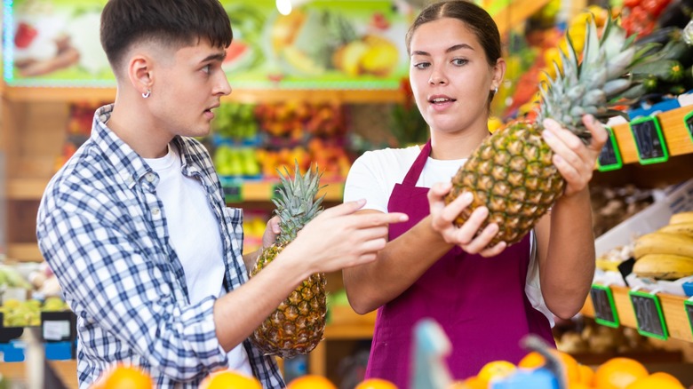 Woman holding a pineapple and showing it to a guy