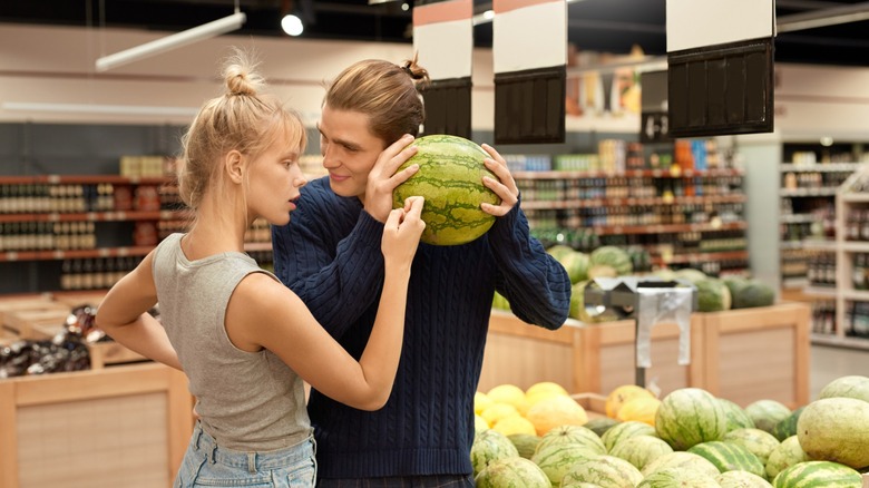 A couple choosing ripe watermelon together by listening to sound check thump while standing in supermarket