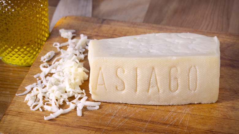 Wedge of Asiago cheese partially grated rests on a cutting board