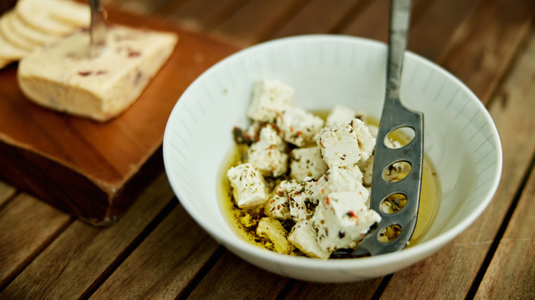 A white bowl of feta cheese cubes with olive oil and spices added