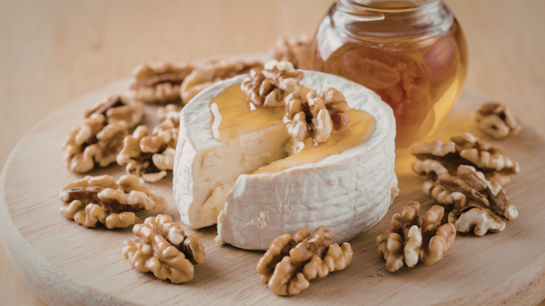 A wheel of goat cheese with a slice cut out of it. Walnut pieces and a drizzle of honey are on top