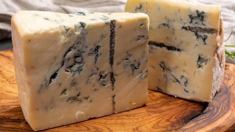 Two wedges of Gorgonzola cheese rest on a wooden board