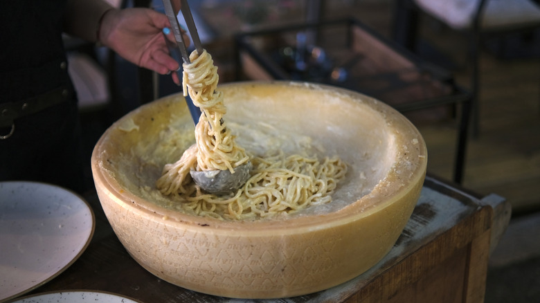 Pasta is being mixed in a hallowed out wheel of Grana Padano cheese
