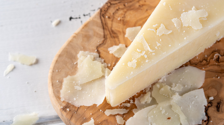A wedge of Pecorino surrounded by flakes of cheese, sitting on a wooden cutting board