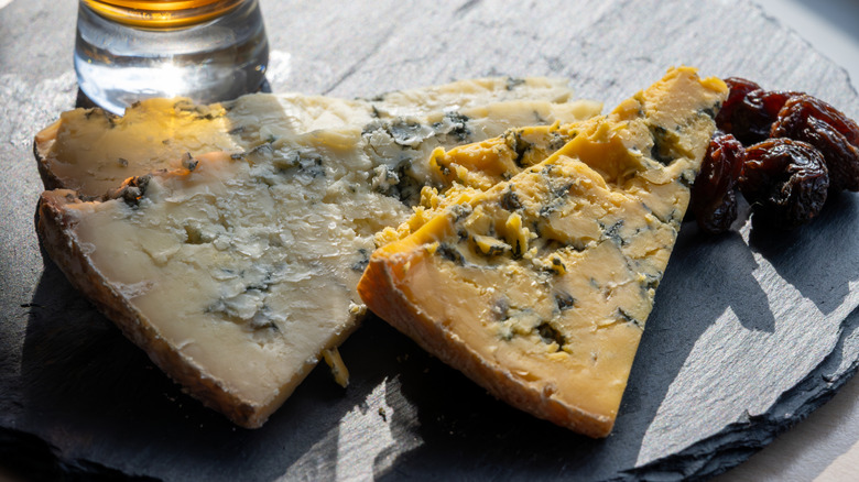 Three wedges of Stilton blue cheese rest on a black plate